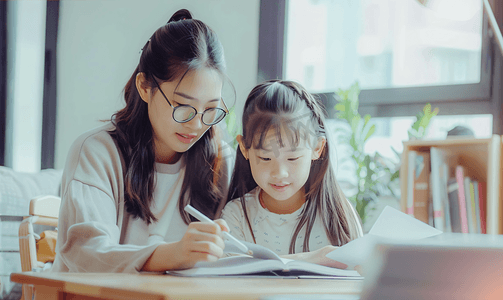 教育交流摄影照片_亚洲人辅导女儿做作业的青年女人