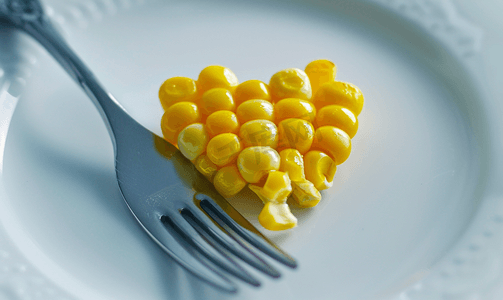 白盘上心形甜玉米和钢叉的特写