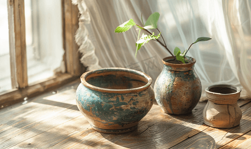 窗户风景画摄影照片_靠近窗户的木桌上的旧粘土陶瓷罐和粘土碗乡村静物画