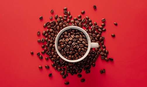 棕色咖啡豆背景摄影照片_红色背景上新鲜烘焙的咖啡豆和白杯的顶视图平躺