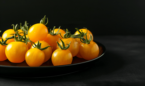 西红柿番茄摄影照片_黑色背景中的黑色盘子上放着漂亮的黄色西红柿