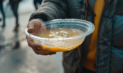 回家吃饭摄影照片_无家可归者在街上用塑料碗吃饭