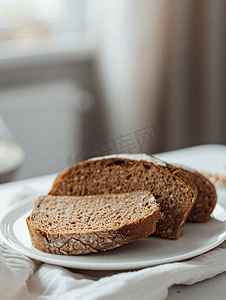 椰蓉馅面包摄影照片_白盘子上超市的黑麦面包美味又漂亮的面包微距照片