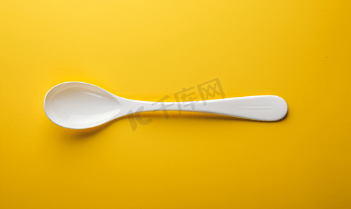 温暖黄色摄影照片_黄色背景上放置的白色塑料勺子