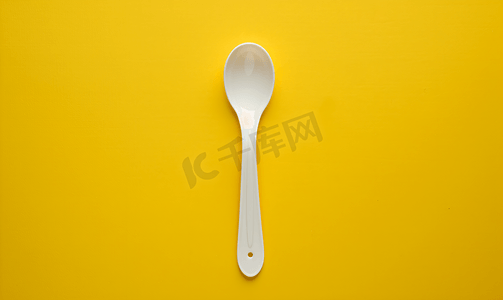 黄色背景上放置的白色塑料勺子