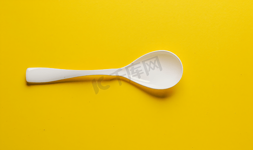 温暖黄色摄影照片_黄色背景上放置的白色塑料勺子
