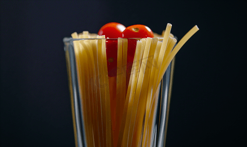 黑色背景上突显的长面条红番茄面条玻璃杯中的意大利面条
