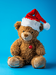 红色庆祝背景摄影照片_蓝色背景中戴着圣诞老人帽子的毛绒泰迪熊