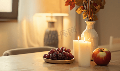 氛围灯光摄影照片_靠近灯的桌子上点燃蜡烛放着一个花瓶里面放着水果、苹果和葡萄