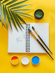 黄色背景上带有水彩调色板画笔和素描本的创意布局