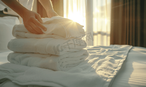 热毛巾敷眼睛摄影照片_客房服务女服务员将一叠白毛巾放在酒店房间的床上