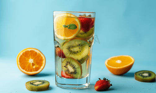 夏季果汁系列摄影照片_蓝色背景中配有奇异果草莓橙片的气泡茶玻璃