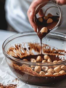 液体巧克力摄影照片_将烤榛子添加到融化的液体巧克力中