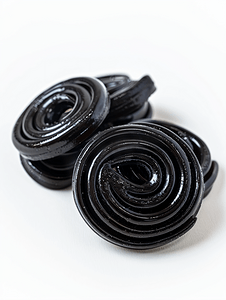 黑色螺旋背景摄影照片_白色上的一些盘绕的黑色甘草糖