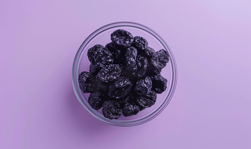 玻璃碗中的干黑李子孤立在紫色渐变上顶视图