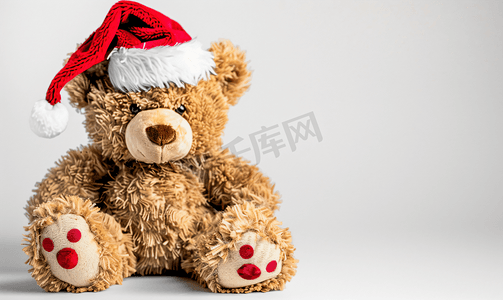动物玩具背景摄影照片_白色背景中戴着圣诞老人帽子的毛绒泰迪熊
