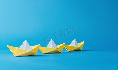 党连引领风帆劲摄影照片_一艘白纸船引领着蓝色背景的三艘黄船