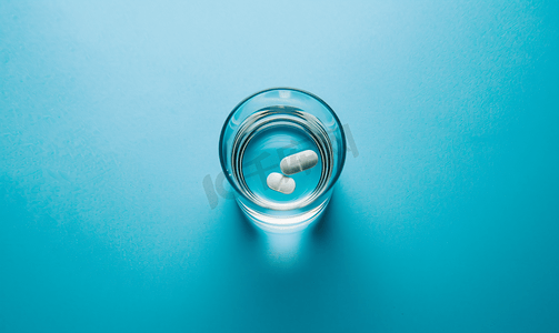药丸溶解在一杯水中背景为蓝色背景顶视图