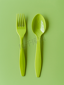 餐饮设计摄影照片_一次性塑料餐具绿色塑料叉子和刀子位于绿色背景表面上