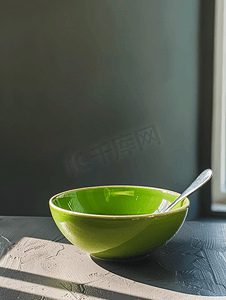 灰棕色桌子上放着绿色碗和钢勺