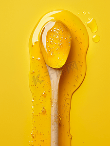 勺子黄色摄影照片_黄色背景上的木制蜂蜜勺子里滴着金色的蜂蜜