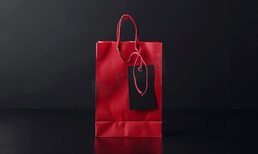 热销爆款标签摄影照片_黑色星期五销售概念标签和深色背景中的红色购物袋