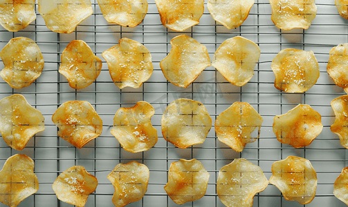 平铺的零食脆皮薯片排列在灰色背景下烘烤的架式烤箱上