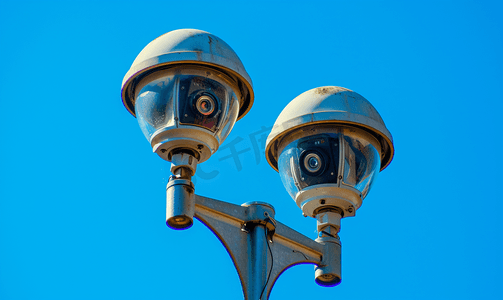 灯杆摄影照片_蓝天背景中路灯杆上的两个旧闭路电视安全监控摄像头