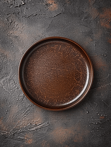 诊疗器具摄影照片_深棕色混凝土背景上一块空的棕色陶瓷盘