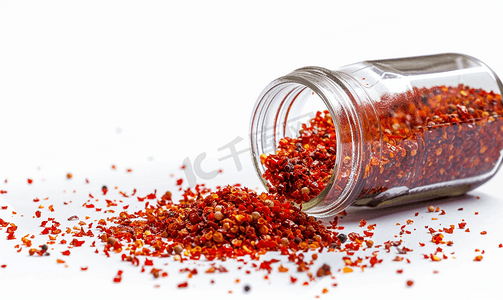 玻璃胡椒罐其侧面掉落有碎红辣椒孤立在白色背景中