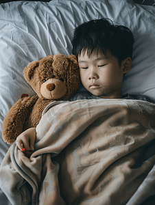 病床上摄影照片_亚洲男孩患流感棕熊躺在病床上治