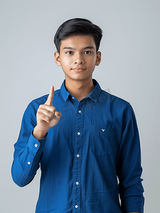 肖像可爱的青年穿着蓝色衬衫用食指指着复制品
