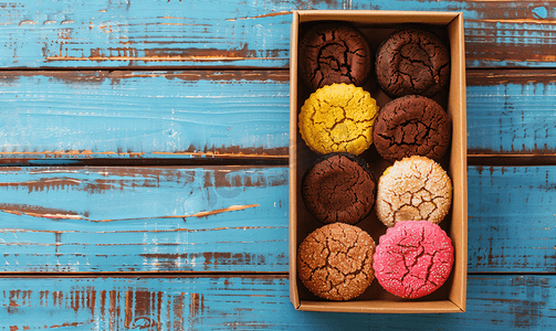 蓝色木质背景的盒子里装着不同颜色的通心粉饼干