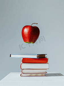 浅色背景中红苹果悬停在一堆书上