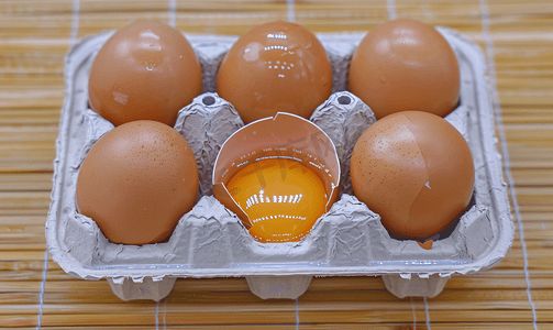 竹桌上塑料盒中六个棕色鸡蛋的特写其中一个破蛋顶视图