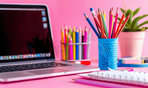 ins风贴纸摄影照片_蓝色支架上的笔记本电脑笔和彩色铅笔以及粉红色上的白色贴纸