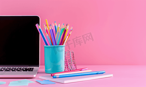 励志卡通小贴纸摄影照片_蓝色支架上的笔记本电脑笔和彩色铅笔以及粉红色上的白色贴纸