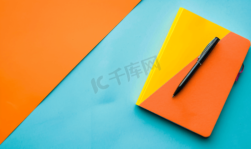 有创造力的摄影照片_有笔的笔记本和蓝色和橙色背景上的彩色笔记