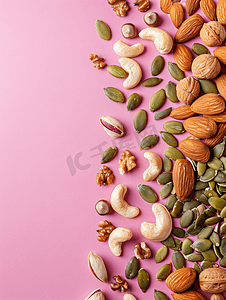 粉红色背景顶视图上不同类型的坚果和南瓜籽