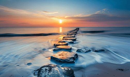 日落景观摄影照片_丹麦海滩上的日落石堤延伸至北海