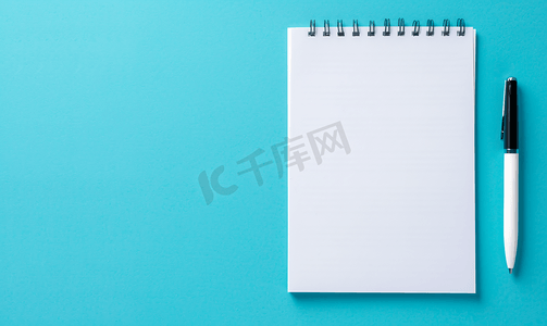 教育笔摄影照片_蓝色背景上带笔的空白便条纸的顶部视图