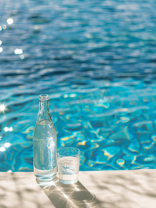 游泳池背景下的白色桌子上放着玻璃杯和瓶子里面装着水