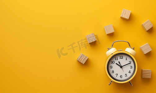 闹钟和日历摄影照片_黄色背景时间概念上的闹钟和木制日历块