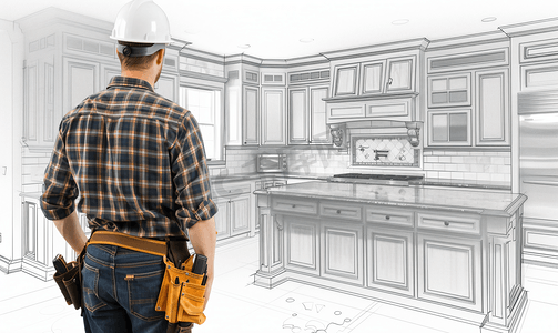 戴着安全帽和工具带的男性承包商看着白色的定制厨房图纸