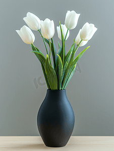 家居室内桌子上黑色花瓶中的人造白色郁金香和绿叶