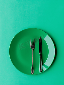 餐具刀和叉摄影照片_空圆形绿色陶瓷板和金属叉刀绿色背景