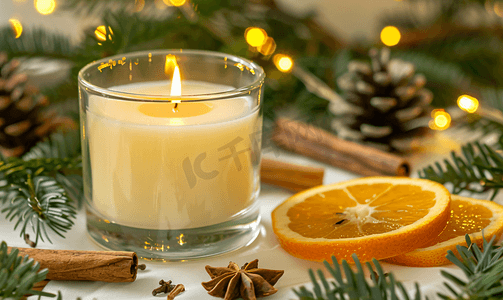 装饰条摄影照片_玻璃杯中的蜡烛上面有橙色肉桂条和冷杉树枝片