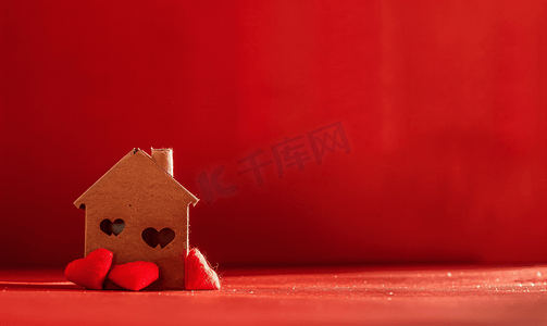 红色背景上带有红心的小玩具屋爱家庭的概念