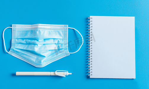 蓝色背景中的一次性医用面罩和螺旋纸记事本