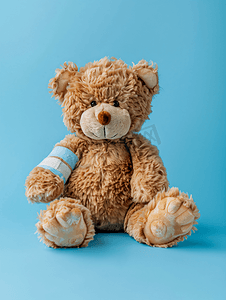 儿童蓝色背景摄影照片_蓝色背景上爪子缠着绷带的棕色泰迪熊